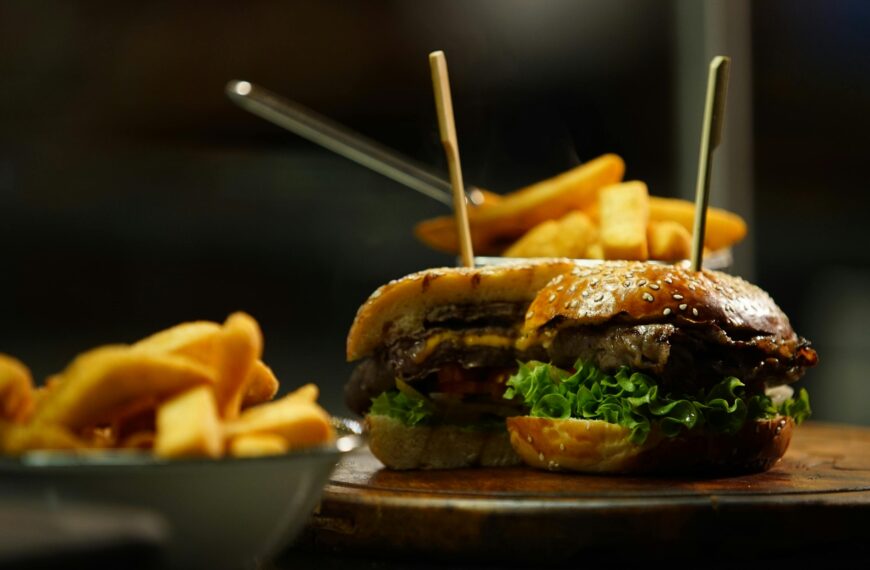 Close-up of a juicy cheeseburger served with crispy fries on a wooden board.